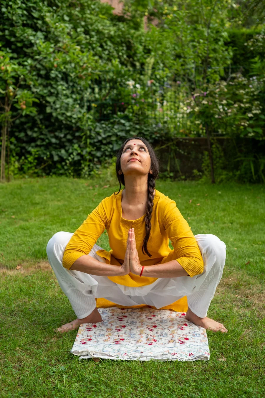 An Indian woman performing a traditional yoga squat with hands clasped in prayer, symbolizing vitality and the 'Yoga for Healthy Ageing' theme.